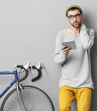 Mann, der auf einem Tablet liest, neben einem Fahrrad vor einer Wand